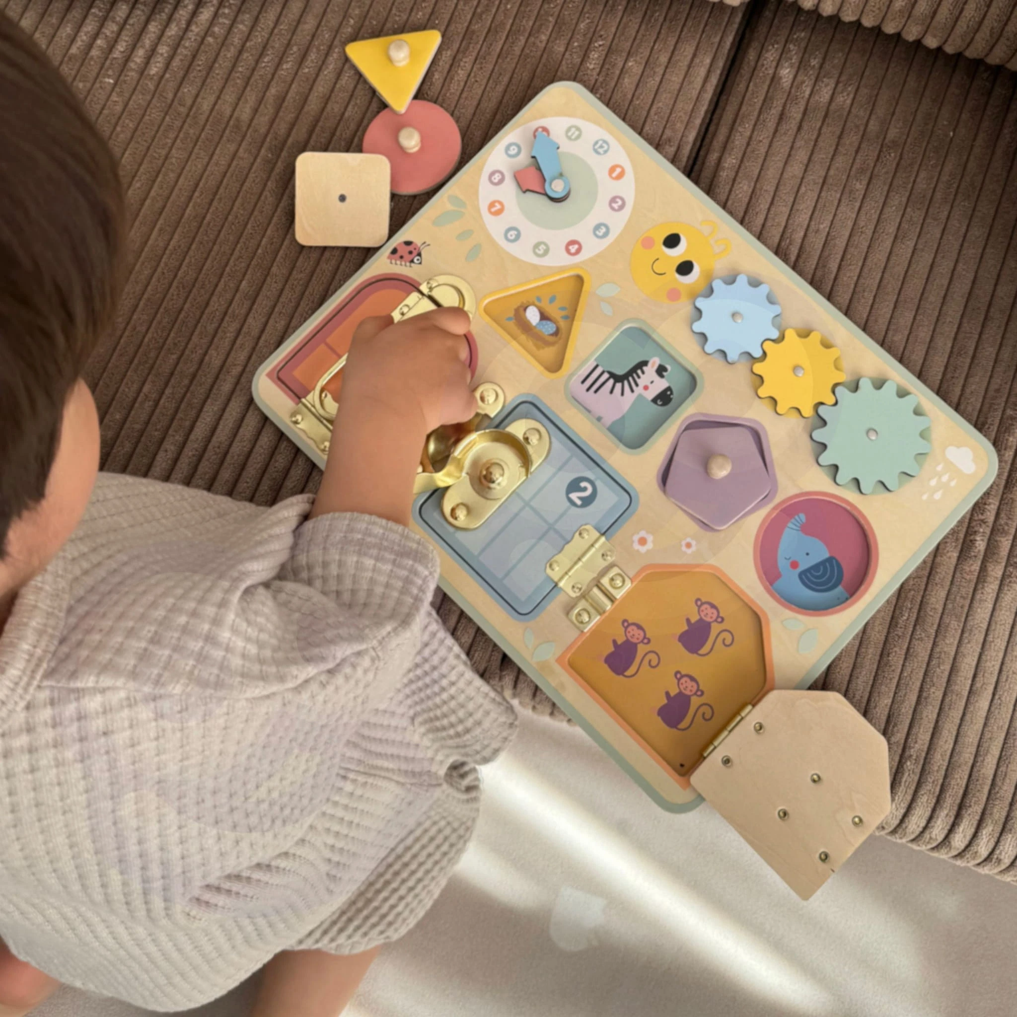 Dziecko bawi się drewnianą tablicą manipulacyjną TOOKY TOY z zamkami, zębatkami, sorterem i zegarem